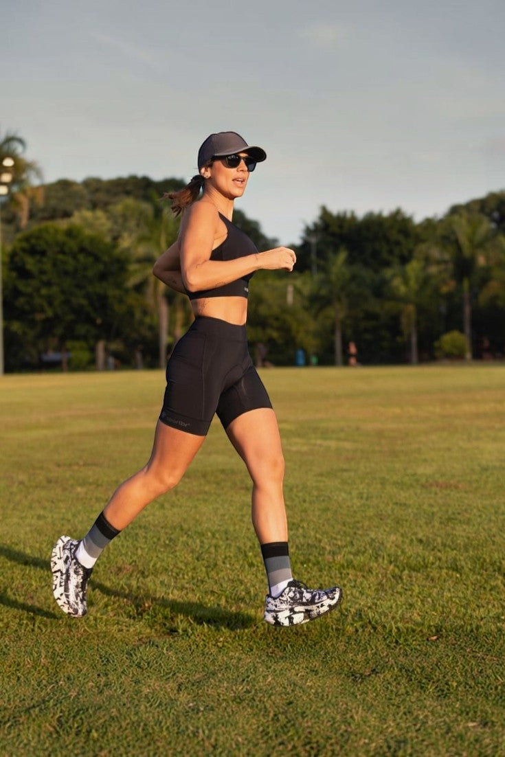 Corredora usando bermuda de compressão preta SPORTBR com bolsos laterais em um parque ao ar livre.