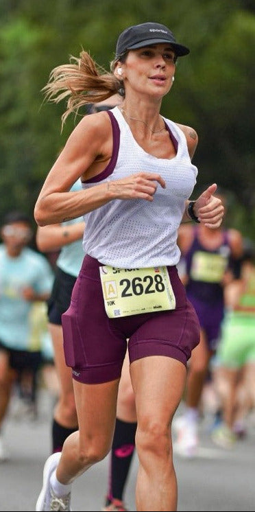Corredora usando bermuda de compressão vinho SPORTBR com bolsos laterais durante prova de corrida de rua ao ar livre