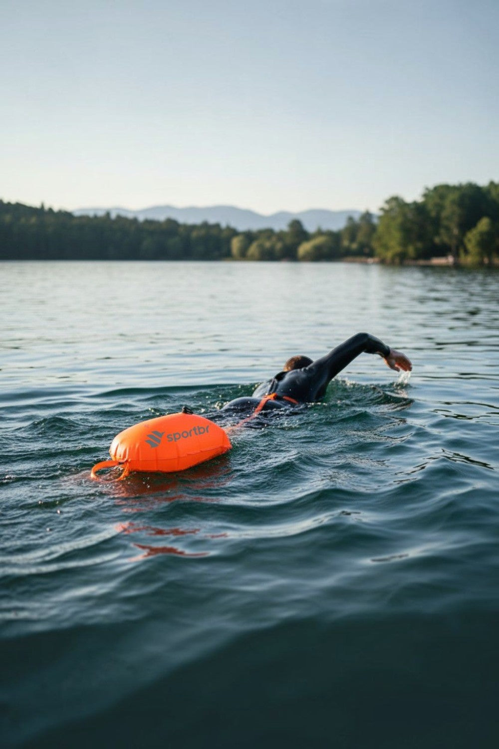 Nadador usando bóia de sinalização laranja SPORTBR de 15L para natação em águas abertas em um lago