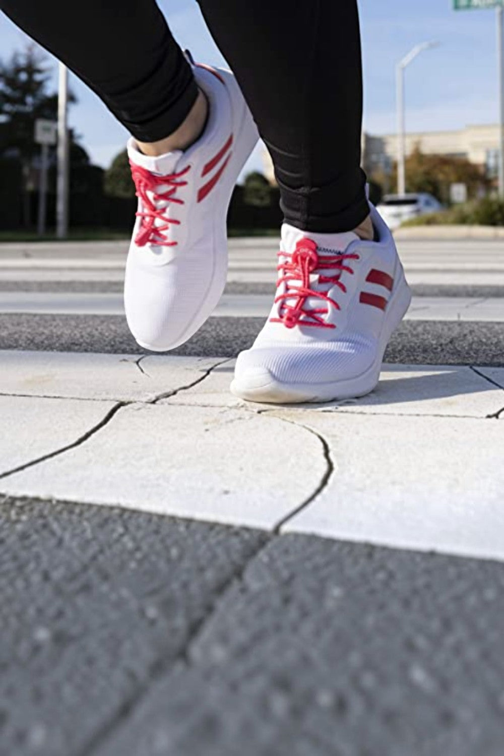 Cadarço elástico Lock Laces rosa pink instalado em tênis branco, usado por corredor em faixa de pedestres SPORTBR