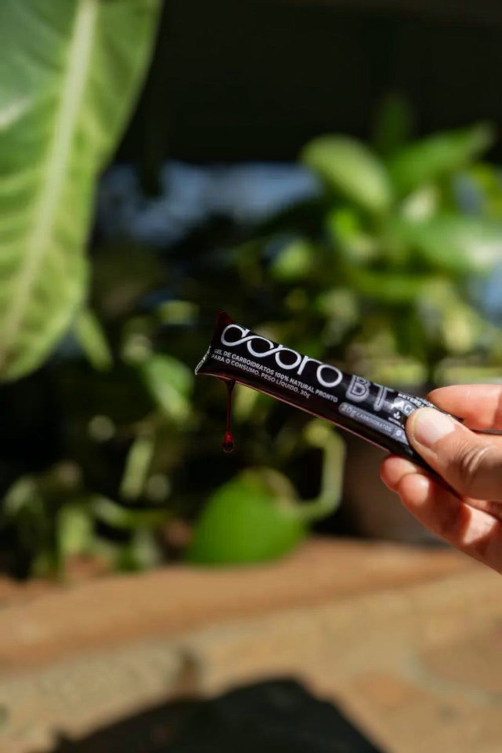 Sachê de gel de carboidrato SPORTBR DOBRO sabor beterraba com acerola sendo aberto ao ar livre com luz solar