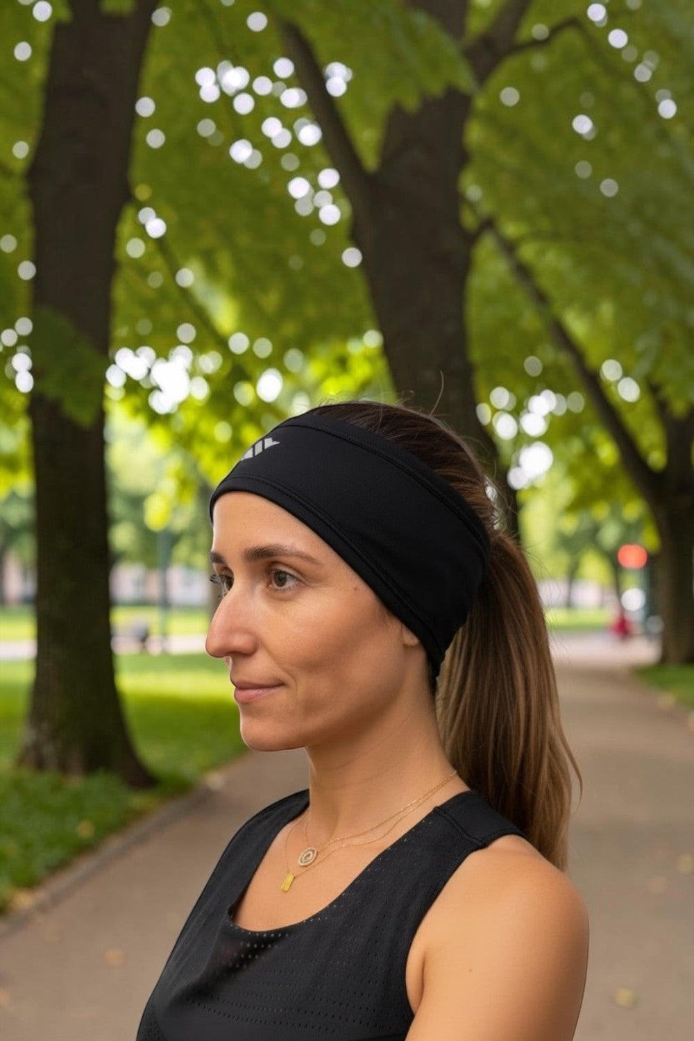 Faixa de cabelo esportiva térmica preta SPORTBR com proteção para orelhas, usada por mulher em parque ao ar livre.