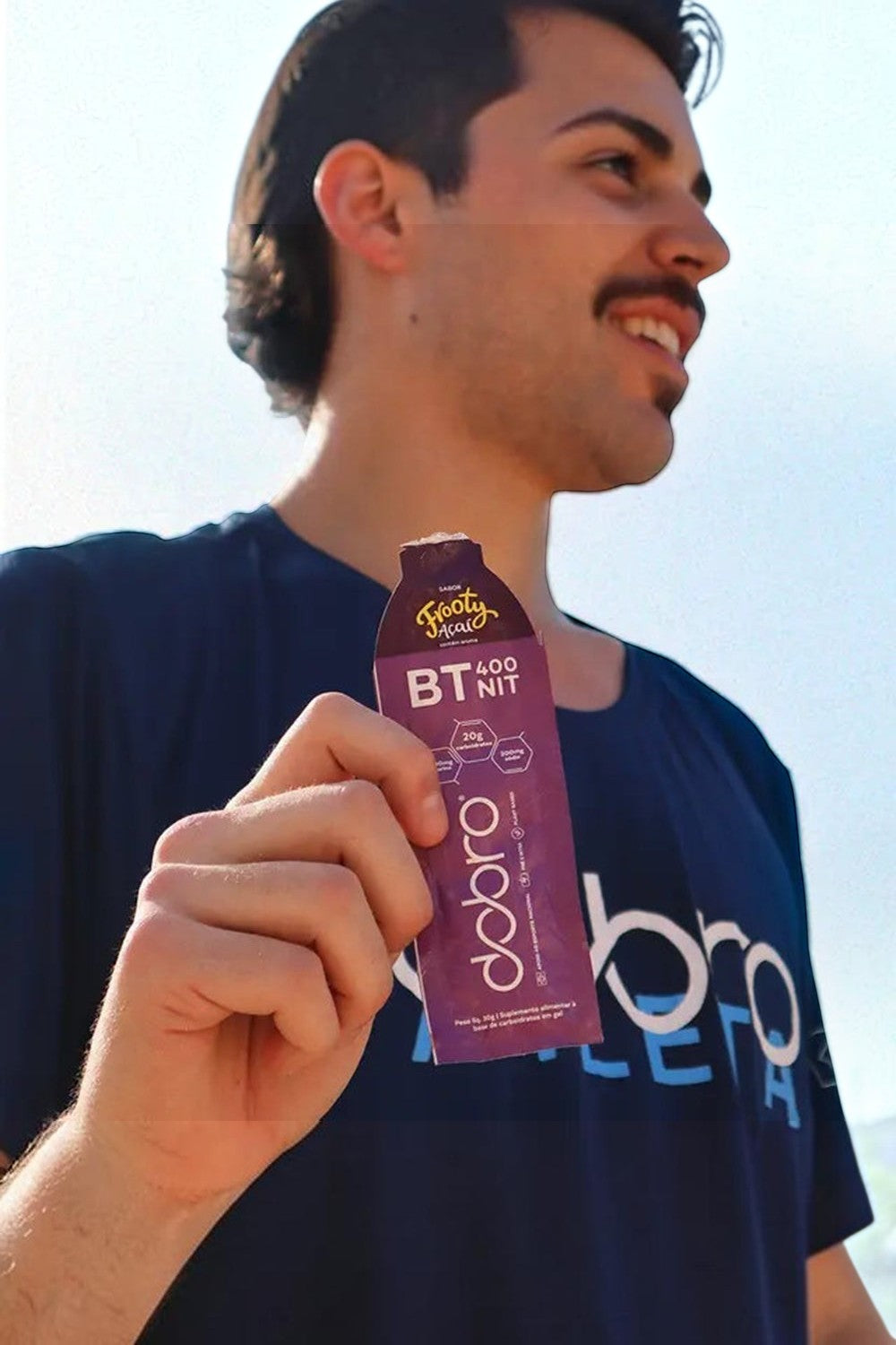 Atleta segurando sachê de gel de carboidrato Dobro BT 400 sabor açaí Frooty, ideal para performance na SPORTBR.