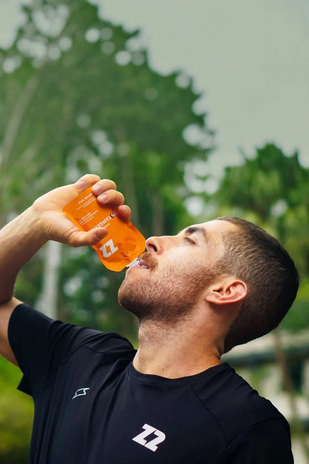 Atleta SPORTBR consumindo sachê de gel de carboidrato Z2 sabor tangerina em embalagem flask durante treino ao ar livre.