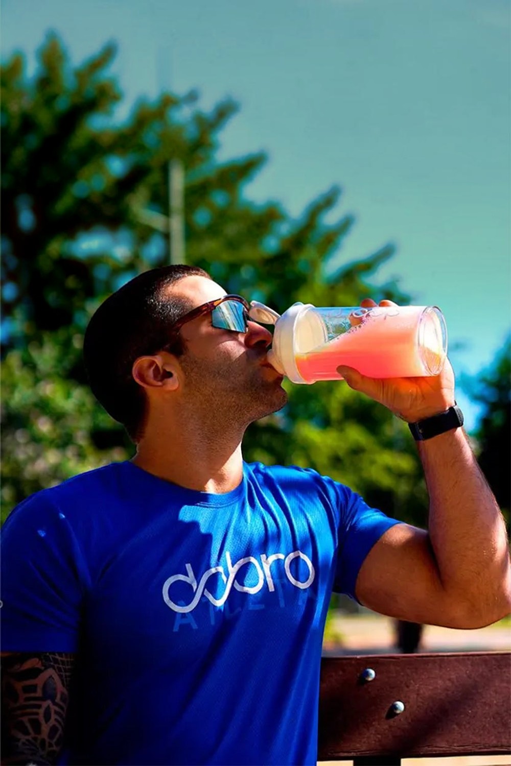 Atleta SPORTBR bebendo HIDRA Eletrólitos sabor laranja e morango em uma coqueteleira ao ar livre