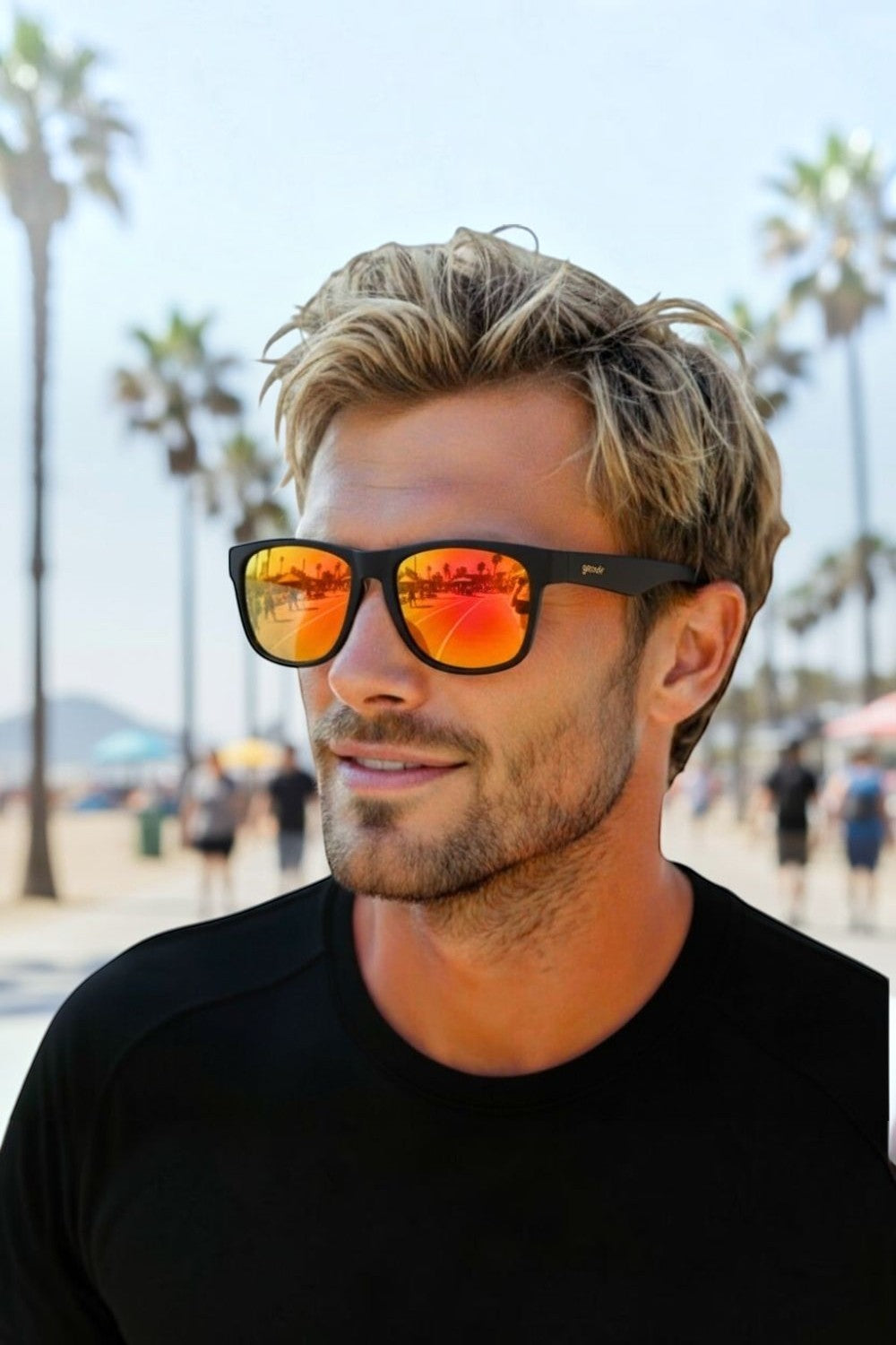 Homem usando óculos de sol SPORTBR Goodr BFG com armação preta e lentes espelhadas amarelas em uma praia ensolarada.