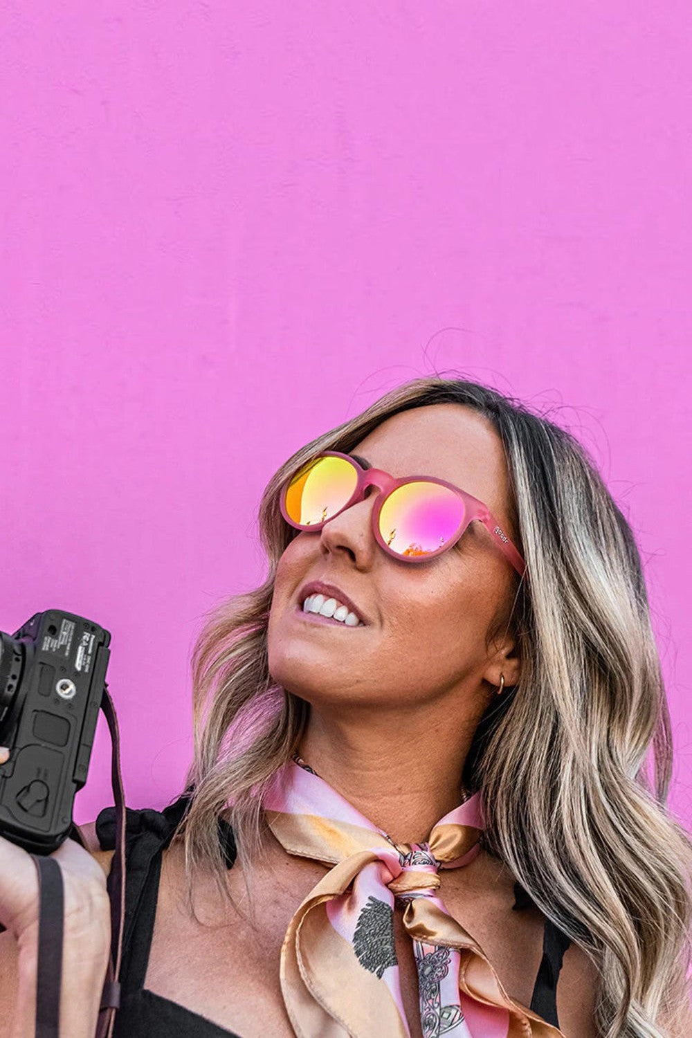 Mulher usando óculos de sol Goodr Influencers Pay Double rosa com lentes espelhadas em fundo rosa, marca SPORTBR.