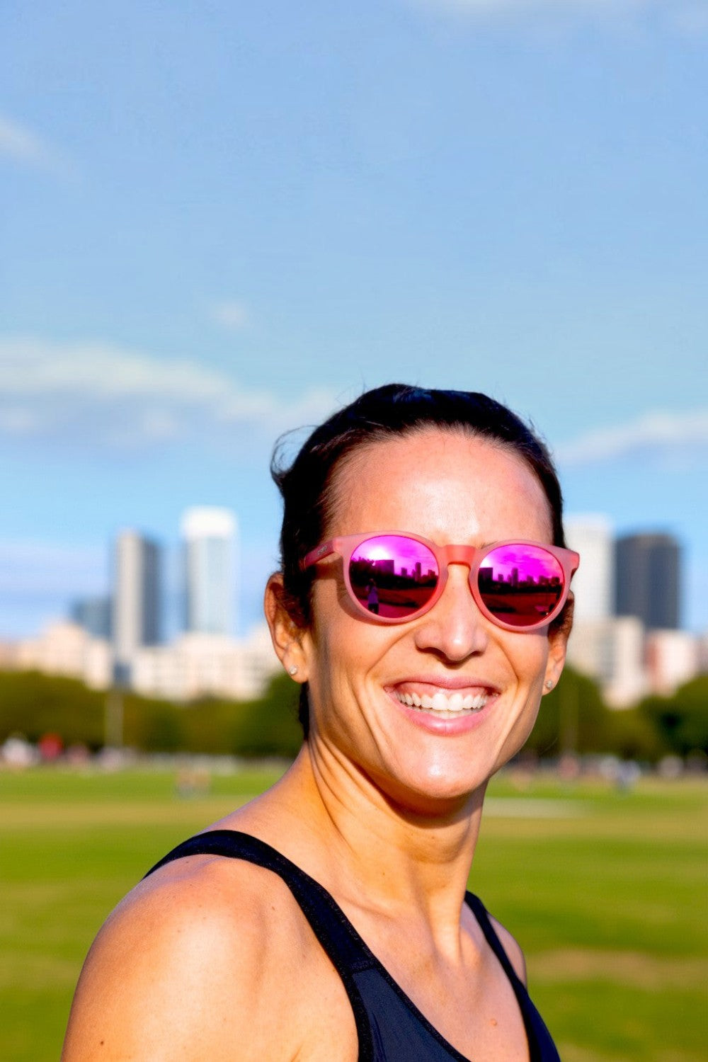 Mulher sorrindo usando óculos de sol rosa Goodr Influencers Pay Double com lentes espelhadas em um parque