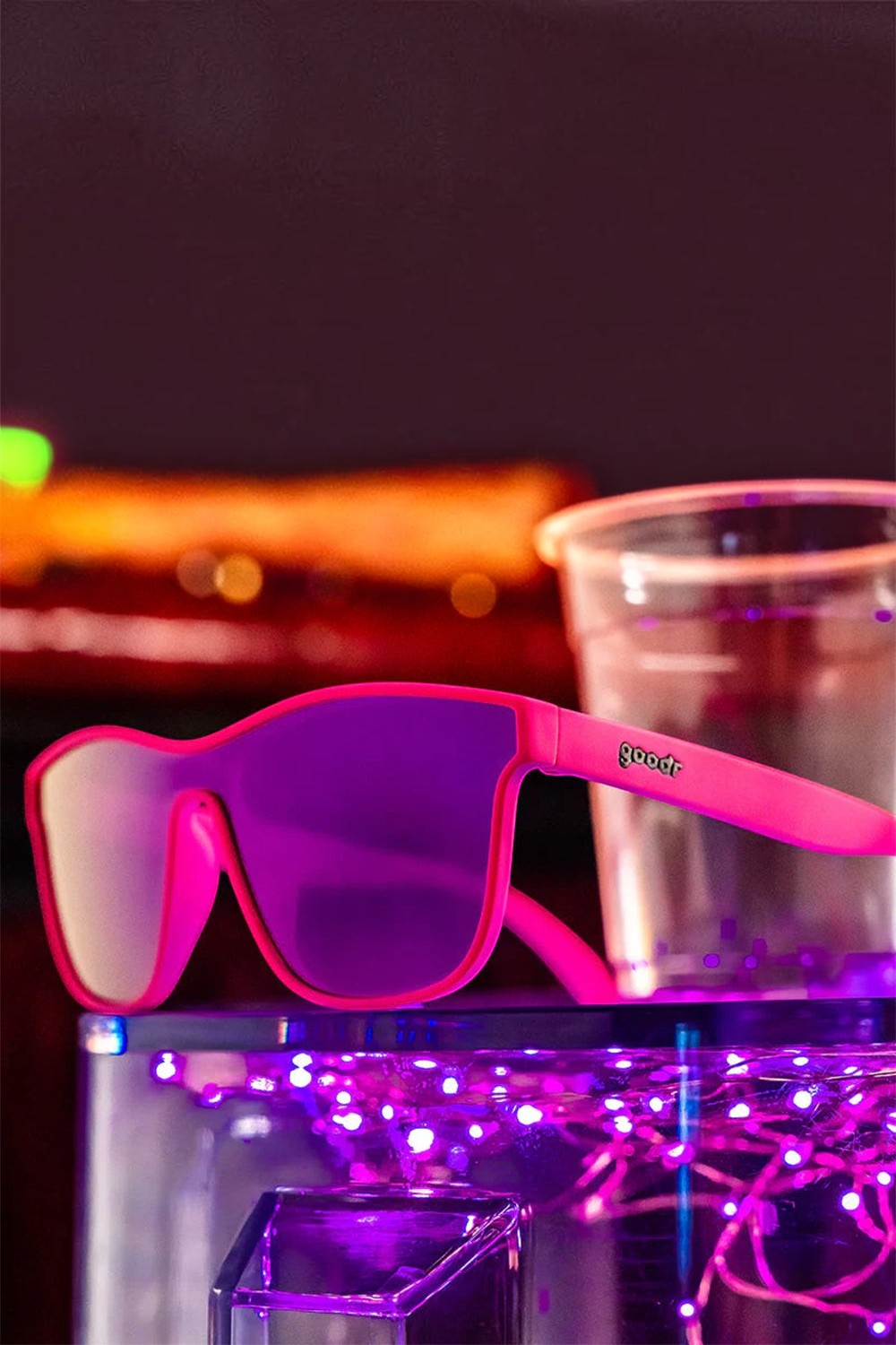 Óculos de sol SPORTBR Goodr rosa com lentes espelhadas roxas, ideal para corrida, sobre superfície iluminada.