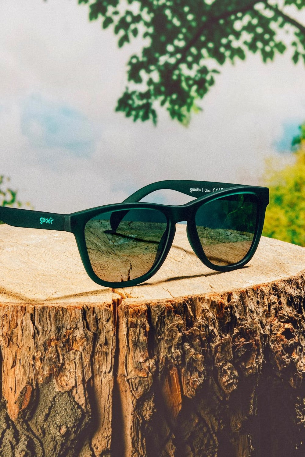 Óculos de sol SPORTBR Goodr 90s Sedan Style Icon verdes com lentes polarizadas sobre um tronco de árvore.