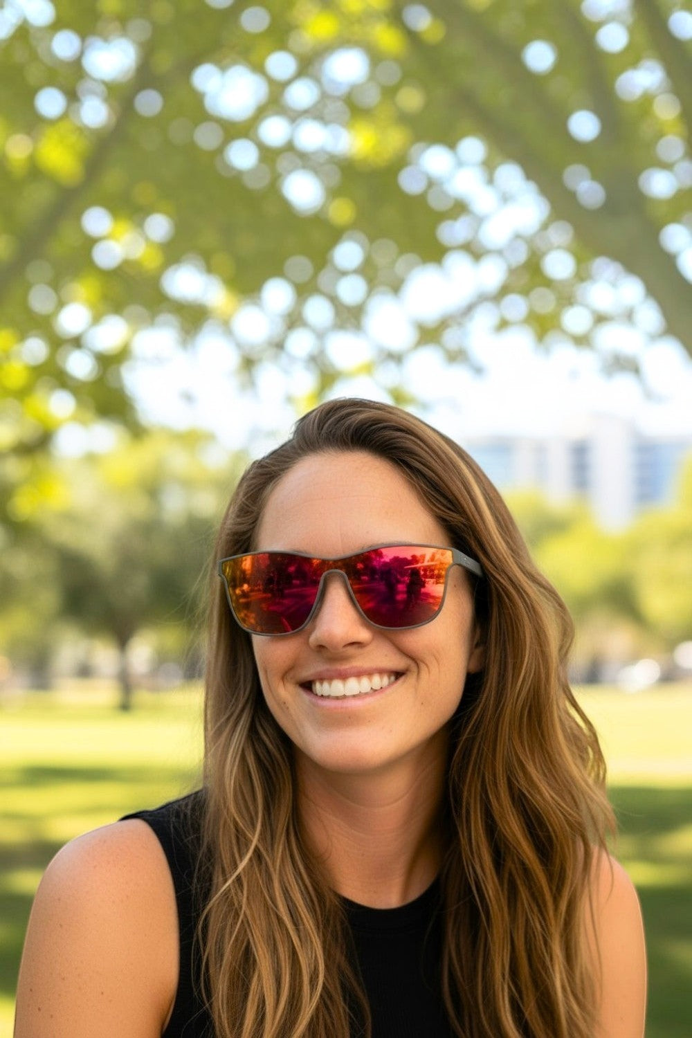 Mulher sorridente usando óculos de sol SPORTBR Goodr Voight-Kampff Vision com armação cinza e lentes espelhadas laranja