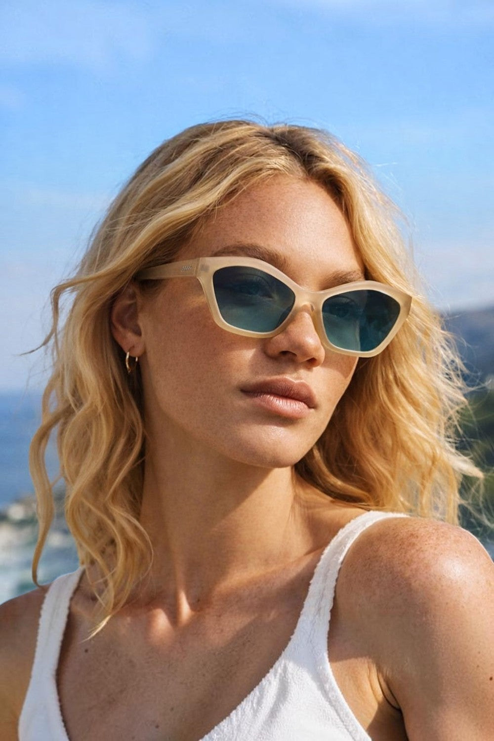 Modelo loira usando óculos de sol SPORTBR Goodr Dulce De Leche Luxe com armação cinza translúcida e lentes verdes.
