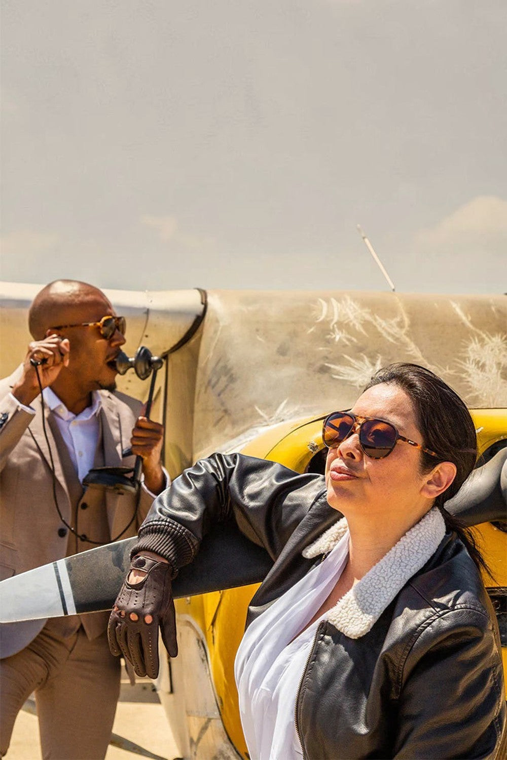 Mulher usando óculos de sol marrom SPORTBR Goodr Amelia Earhart Ghosted Me com lentes polarizadas ao lado de avião