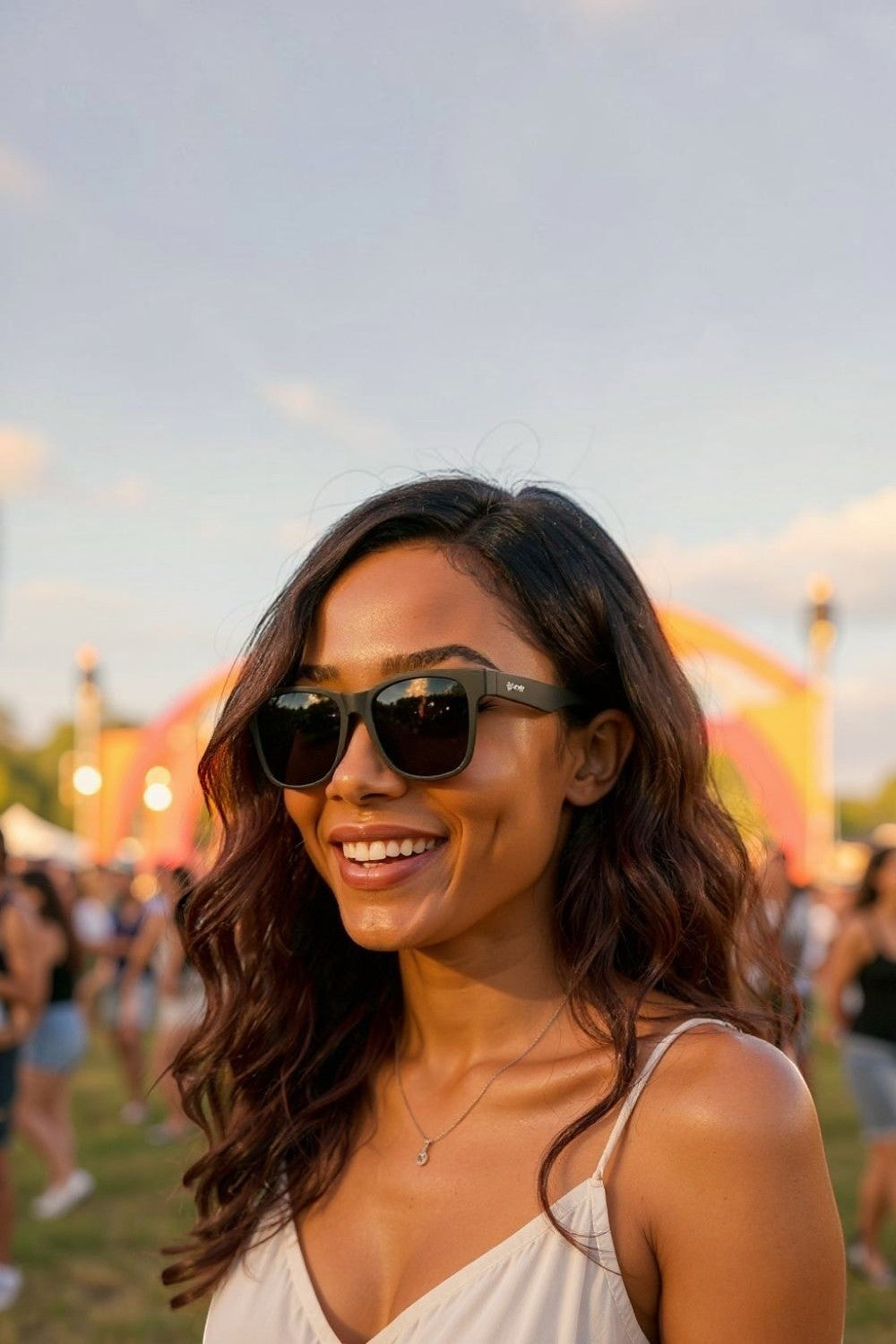 Mulher sorridente usando óculos de sol pretos Goodr Hooked On Onyx com lentes polarizadas em um evento ao ar livre.