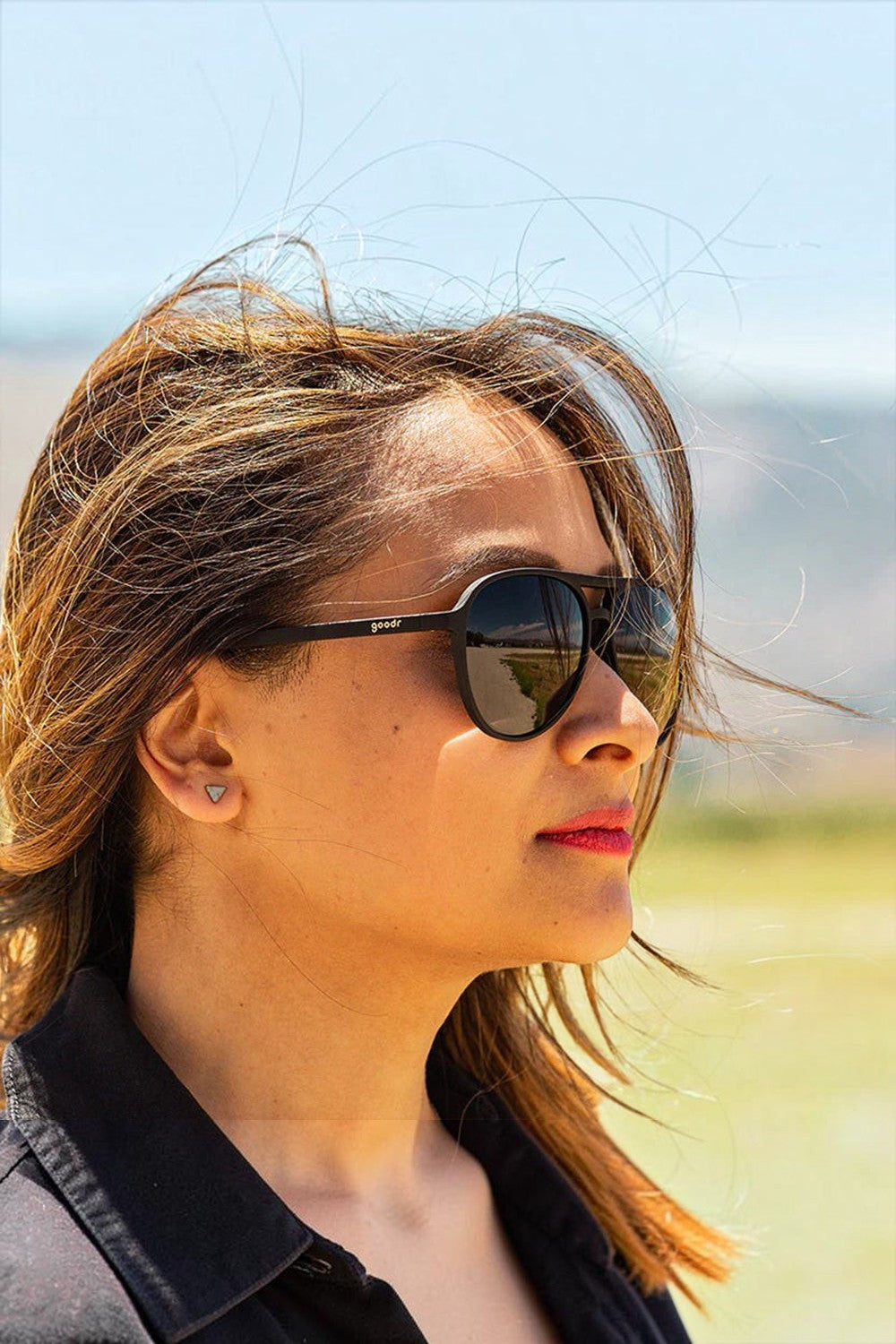 Mulher usando óculos de sol esportivos pretos Goodr Operation: Blackout com lentes polarizadas em dia ensolarado.