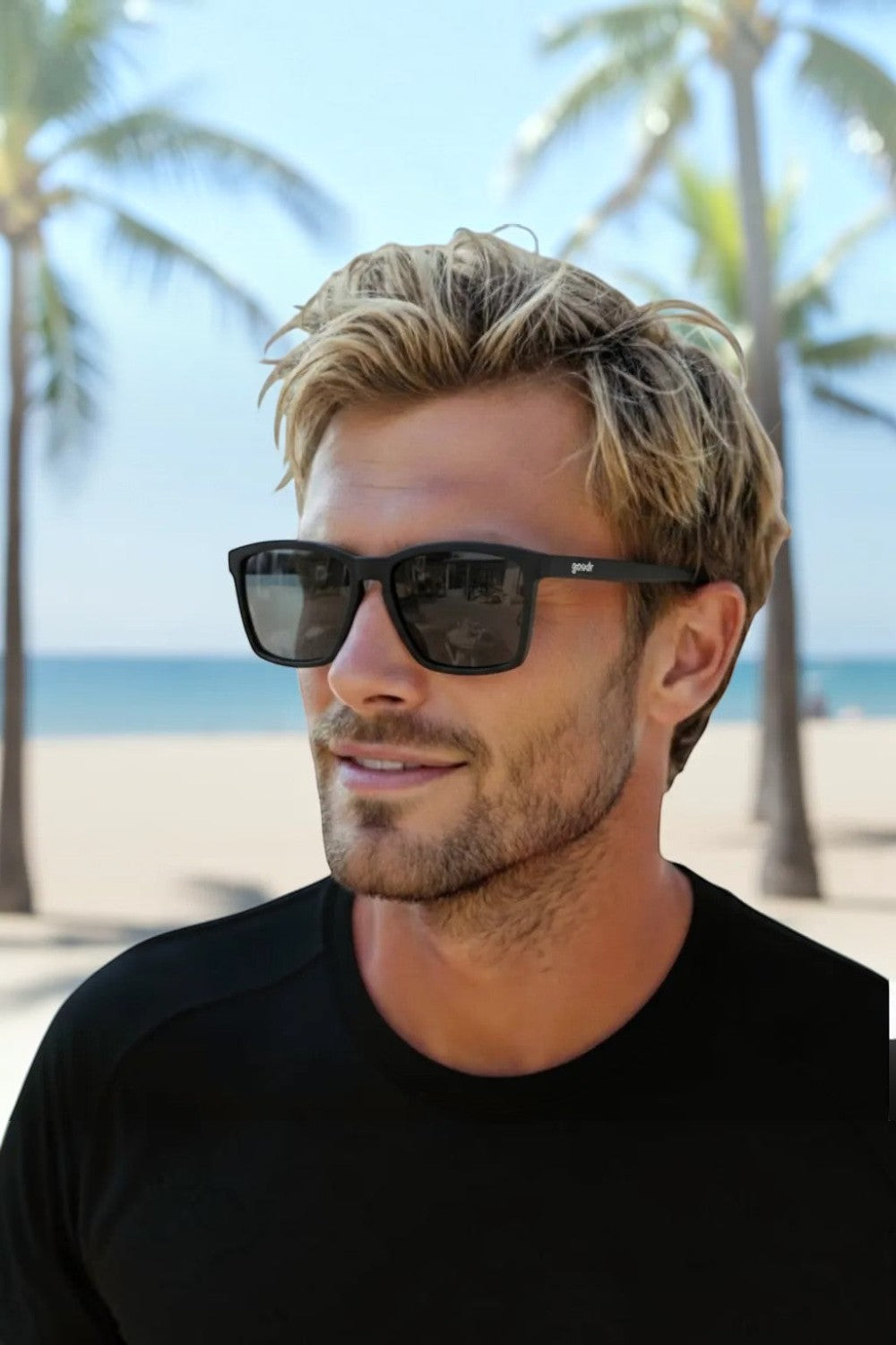 Homem usando óculos de sol esportivos pretos Goodr Get On My Level com lentes polarizadas em um cenário de praia.