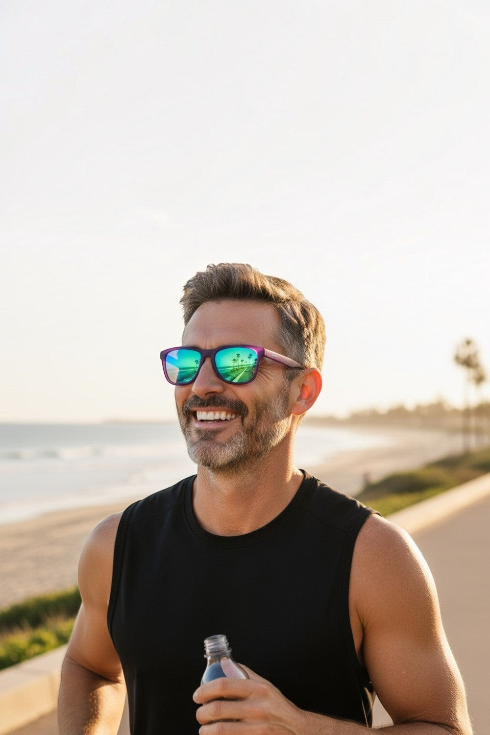 Homem sorridente usando óculos de sol SPORTBR Goodr roxos com lentes espelhadas verdes durante corrida na praia.