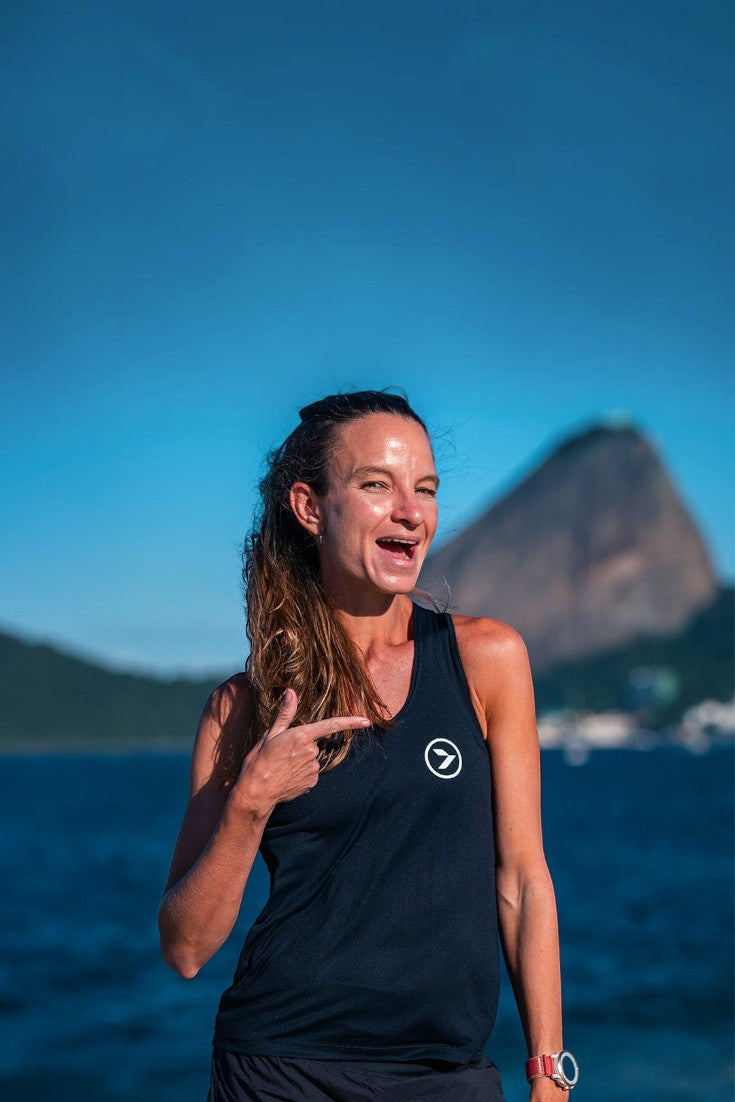 Mulher sorridente vestindo regata preta de poliamida SPORTBR Julia Sette Pace em cenário ao ar livre com montanha