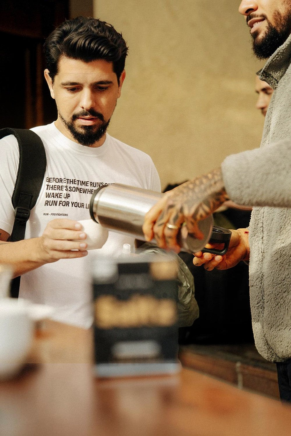 Homem servindo bebida quente em xícara, produto SPORTBR Saltz Café para reposição eletrolítica em sachês.