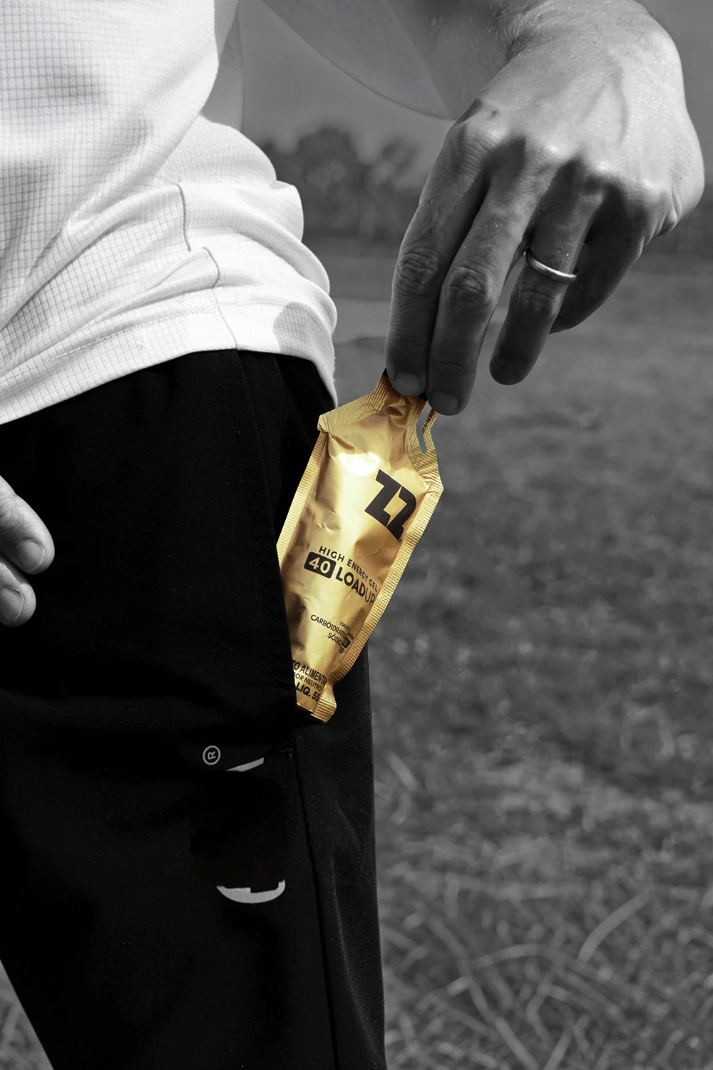 Sachê de gel de carboidrato Sportbr Z2 LoadUp dourado sendo retirado do bolso de shorts esportivo preto.