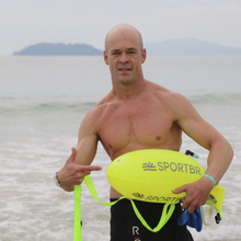 Homem utilizando bóia sinalizadora amarela na praia.