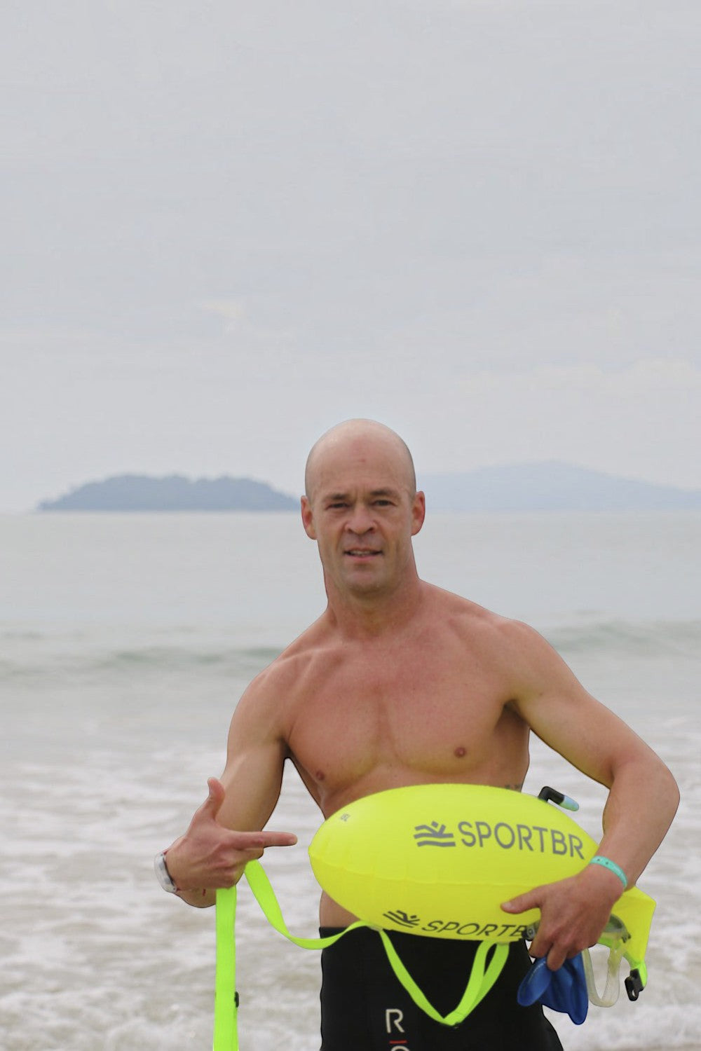 Nadador segurando bóia de sinalização amarela SPORTBR de 15L na praia para natação em águas abertas