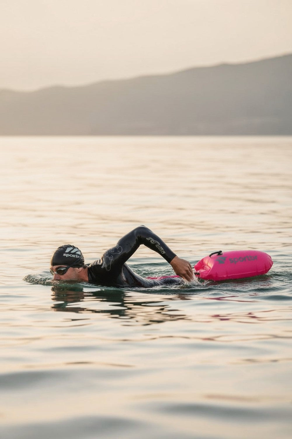 Nadador com roupa de neoprene usando bóia de sinalização rosa SPORTBR em mar aberto para maior segurança