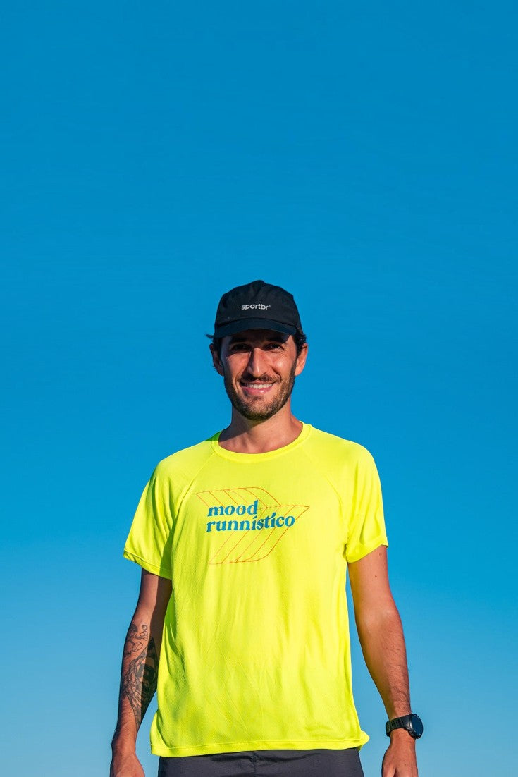 Homem vestindo camiseta esportiva SPORTBR amarela neon com estampa Mood Runístico e boné preto ao ar livre