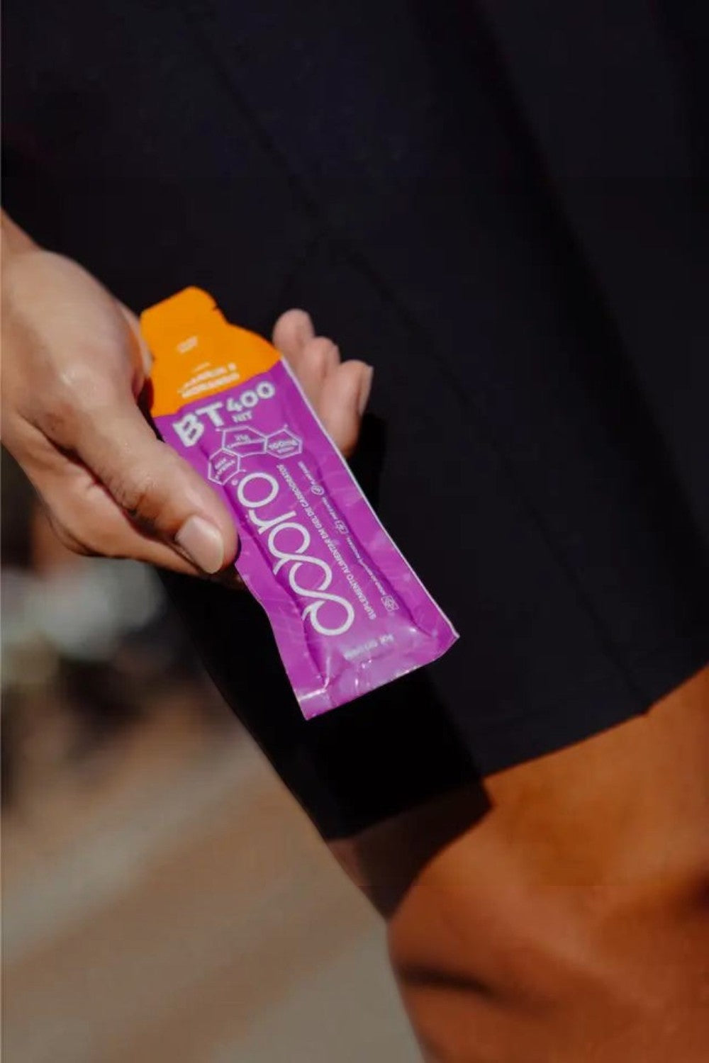 Sachê de gel de carboidrato SPORTBR Dobro sabor laranja e morango, com 400mg de nitrato, sendo segurado por um atleta.