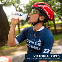 Mulher ciclista bebendo bebida energética Z2 Iced Tangerine de uma garrafa SPORTBR. Ela usa capacete vermelho S-Works e jersey azul.