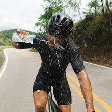 Ciclista SPORTBR em treino intenso, bebendo água para se refrescar e manter a performance. Roupa preta, capacete preto.