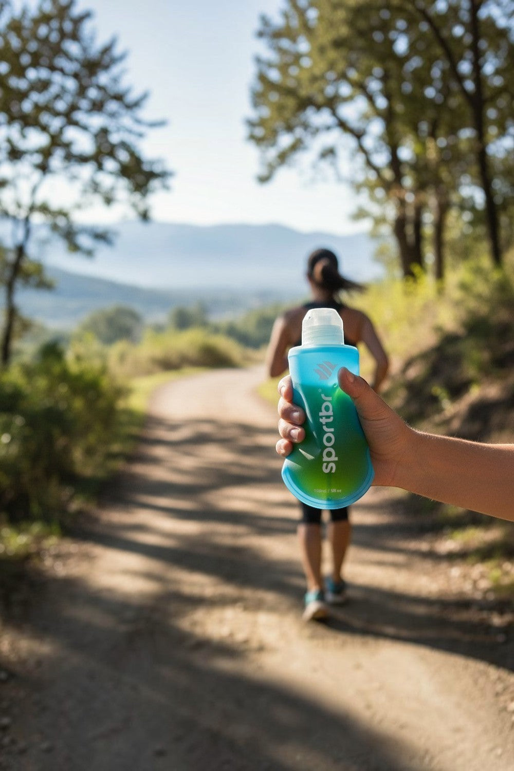 Garrafa flexível SPORTBR azul de 150ml para gel de corrida, sendo segurada por um atleta em uma trilha ao ar livre.