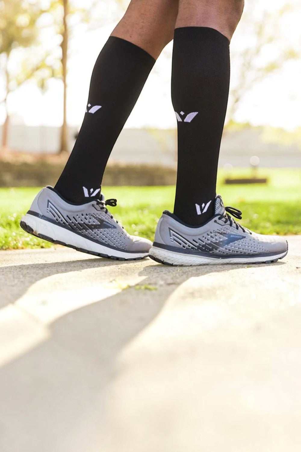 Meia de compressão preta SPORTBR Swiftwick Aspire de cano alto em corredor com tênis cinza em ambiente externo.