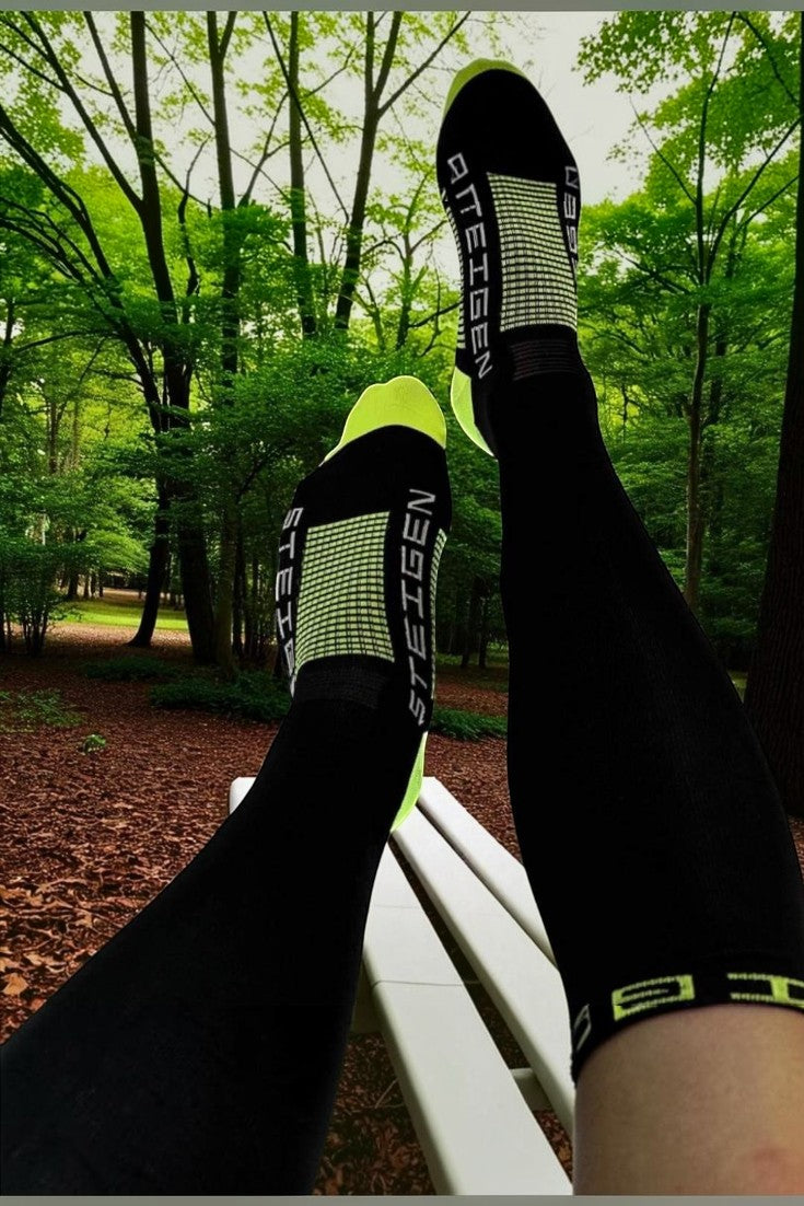 Meia esportiva de cano alto SPORTBR preta com detalhes em verde neon, usada por corredor em parque arborizado.
