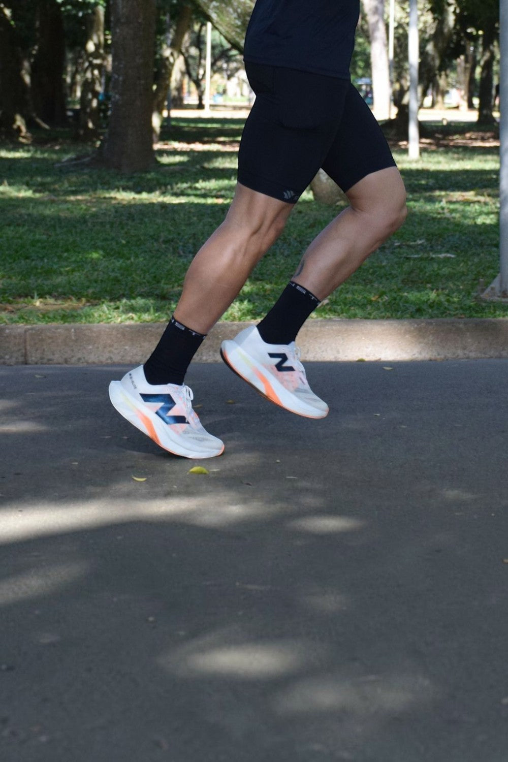 Corredor usando meia SPORTBR Steigen cano alto preta, tênis de corrida e bermuda em um parque ao ar livre.