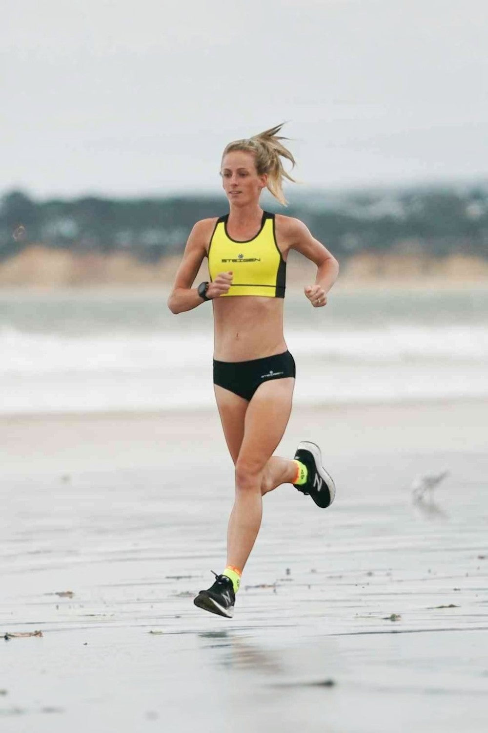 Corredora na praia usando meia SPORTBR Steigen cano baixo na cor amarelo flúor durante treino de corrida