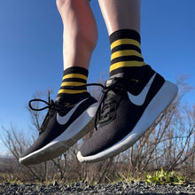 Meias esportivas Steigen cano médio listradas em preto e amarelo, com tênis Nike preto.