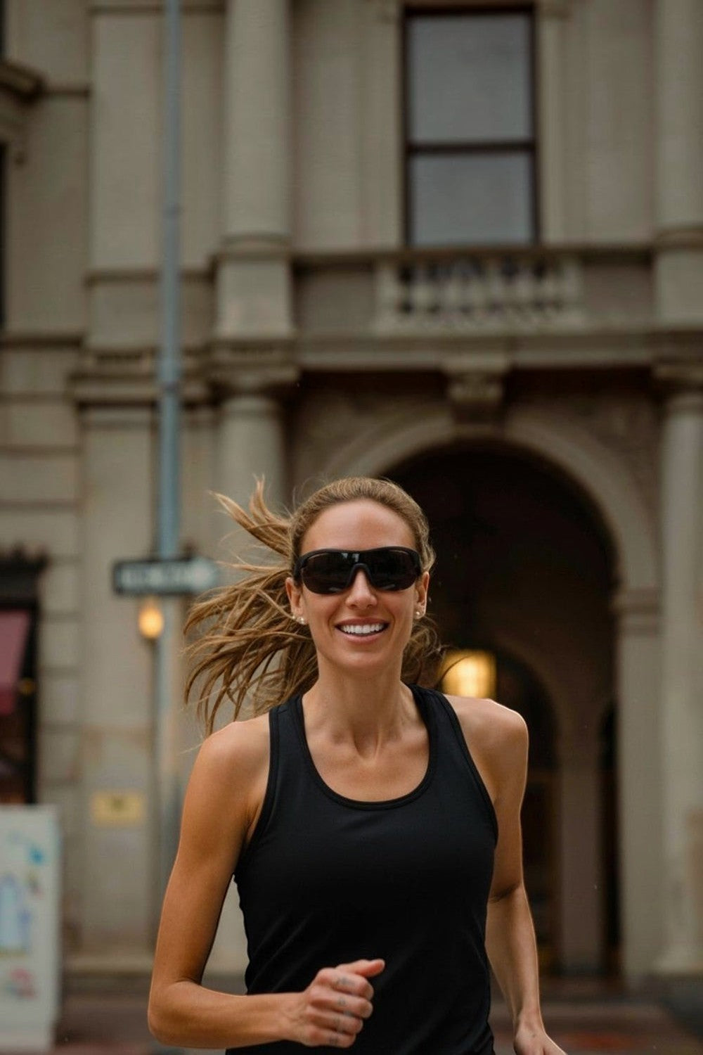 Mulher correndo na rua usando óculos de sol esportivos pretos SPORTBR Goodr When The World Blurs com lentes polarizadas