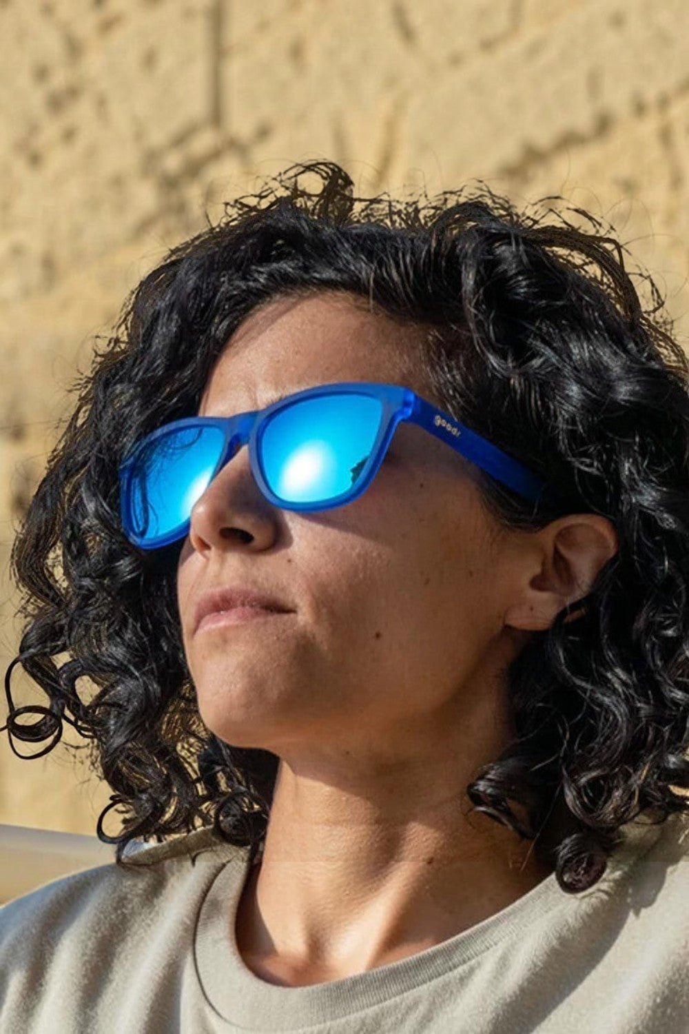 Mulher usando óculos de sol SPORTBR Goodr Falkor's Fever Dream com armação e lentes espelhadas azuis para corrida.