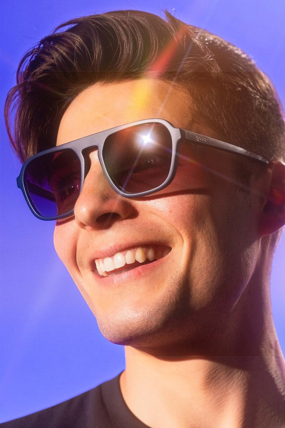 Homem sorrindo usando óculos de sol SPORTBR Goodr Deja Vu Daydream com armação azul e lentes roxas polarizadas.