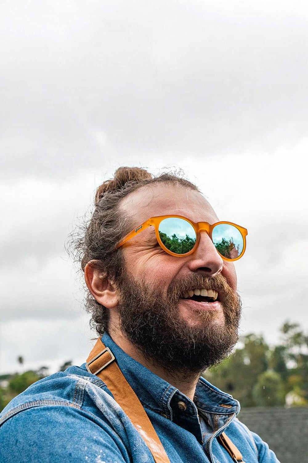 Homem usando óculos de sol SPORTBR Goodr Freshly Baked Man Buns com armação laranja e lentes espelhadas azuis.