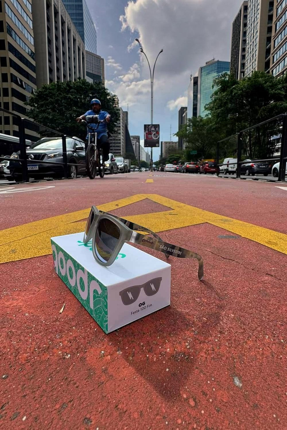 Óculos de sol SPORTBR goodr Festa 100 Fim São Silvestre cinza sobre caixa na Avenida Paulista para corrida.