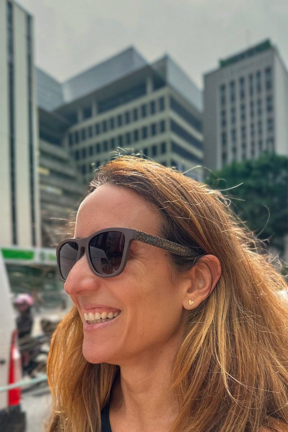 Mulher sorrindo usando óculos de sol marrom SPORTBR Goodr Feliz Pace Novo São Silvestre com detalhes de brigadeiros.