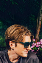 Homem usando óculos de sol Goodr verdes modelo 90s Sedan Style Icon com lentes polarizadas em ambiente externo.