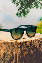 Óculos de sol SPORTBR Goodr 90s Sedan Style Icon verdes com lentes polarizadas sobre um tronco de árvore.
