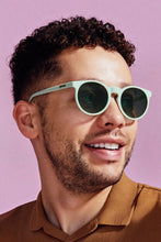 Homem usando óculos de sol Goodr Incognito Plant Parent com armação verde e lentes polarizadas em fundo rosa.