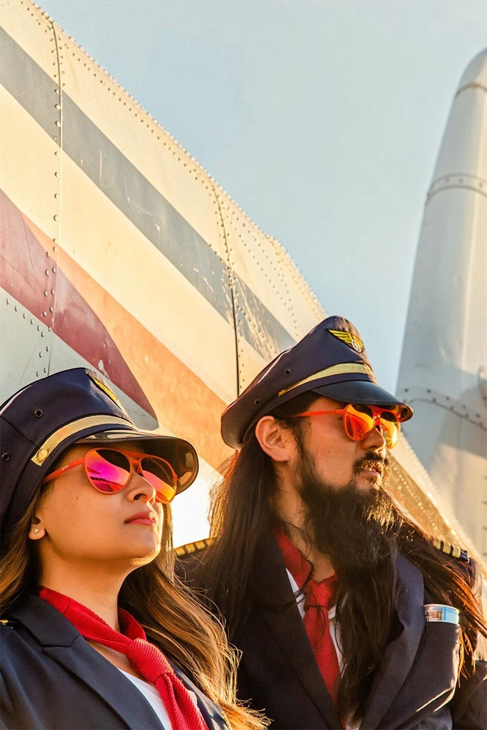 Dois modelos vestidos de pilotos usando óculos de sol SPORTBR Goodr Captain Blunt's Red-Eye com lentes rosas espelhadas