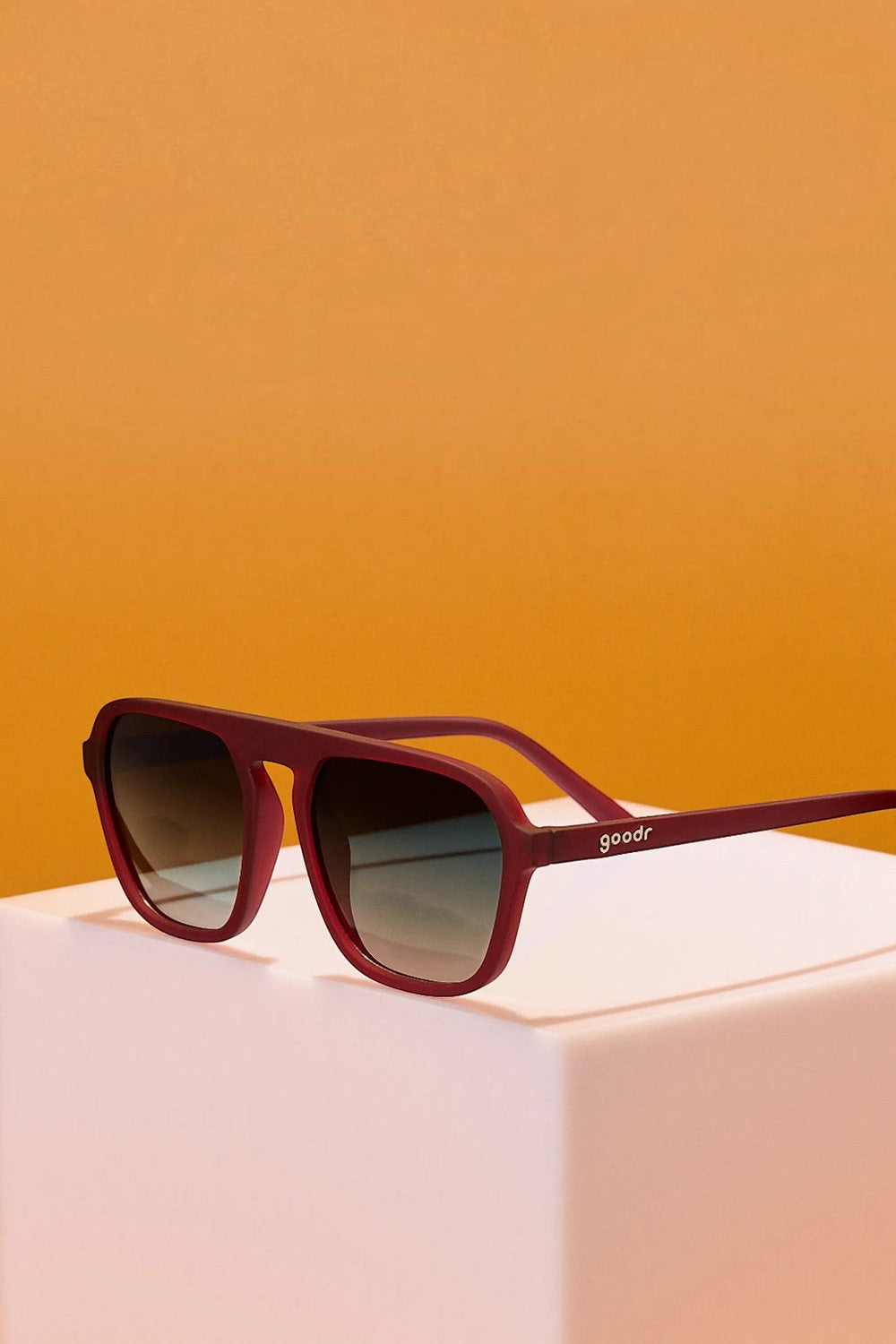 Óculos de sol SPORTBR Goodr Conversation Pit com armação vinho e lentes verdes polarizadas em suporte branco.
