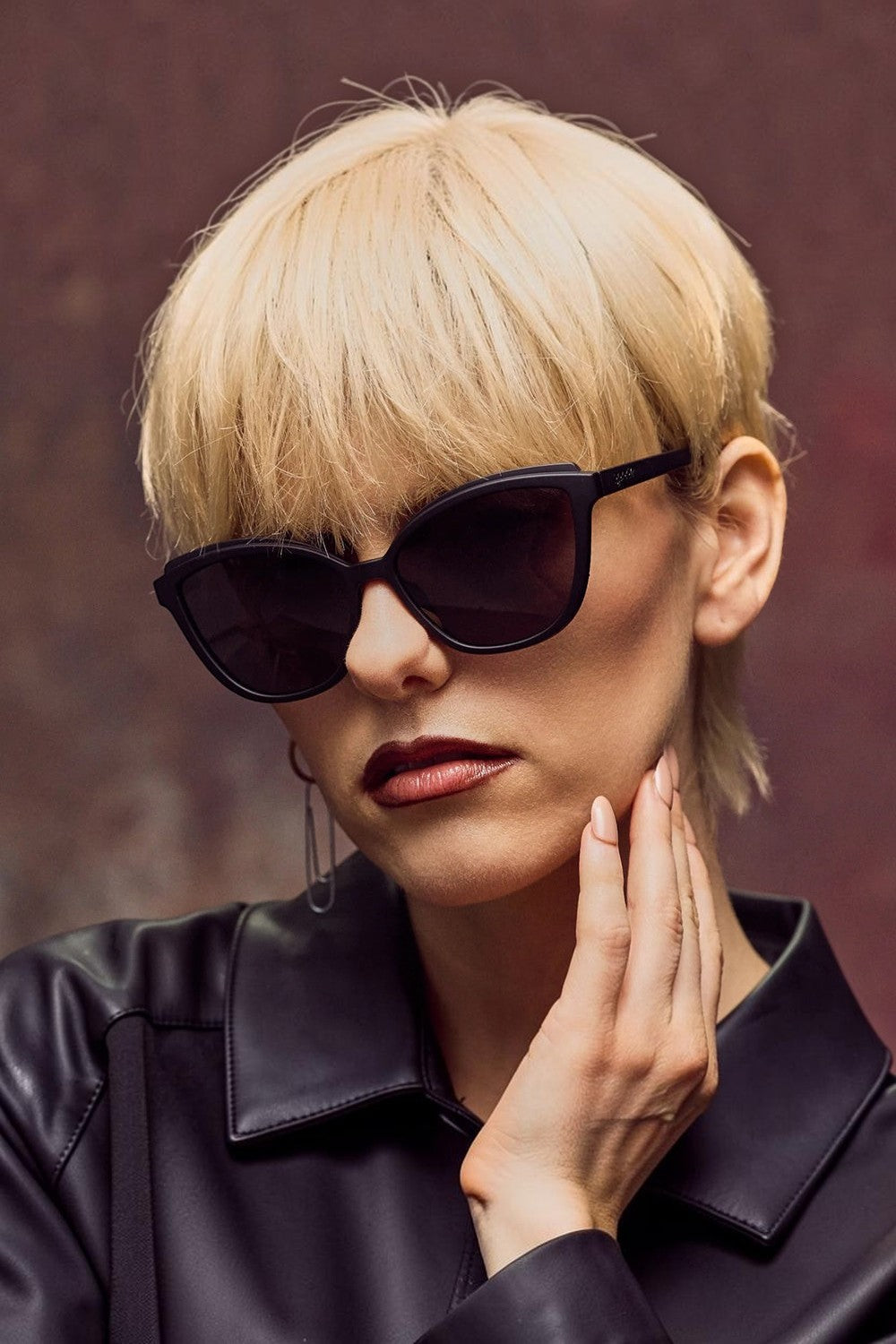 Modelo loira usando óculos de sol SPORTBR Goodr Not a Carbon Copy com armação preta estilo cat-eye e lentes escuras.