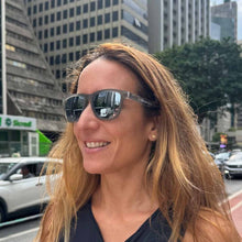 Mulher sorrindo usando óculos de sol cinza espelhados polarizados da SPORTBR Festa 100 Fim São Silvestre, com armação cinza flexível e detalhes da São Silvestre.